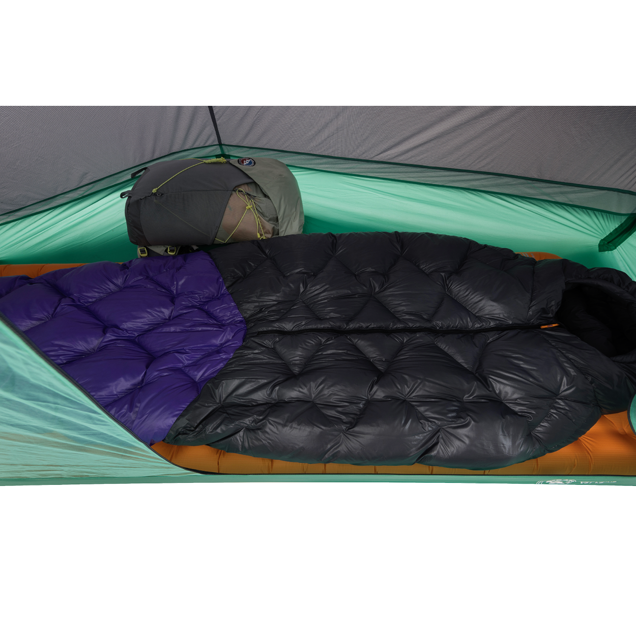 Two sleeping bags—one all black and one with a purple section—are side by side inside a green Big Agnes Returns Pitchpine VST 1.5 tent, set up with an orange sleeping pad beneath and a gray backpack at the head for an ultralight shelter setup.