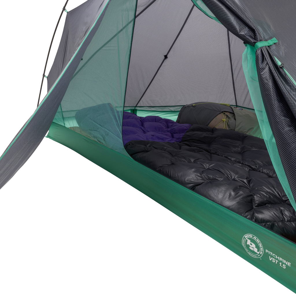A close-up of the Big Agnes Pitchpine VST 1.5 tent interior reveals two sleeping bags side by side on the floor, with mesh sides and a partially open door in this ultralight green and grey shelter.