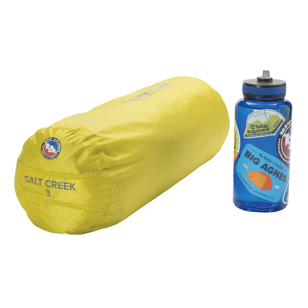 A yellow Big Agnes Returns Salt Creek 3 tent storage bag sits beside a blue water bottle with outdoor-themed stickers on a white background.