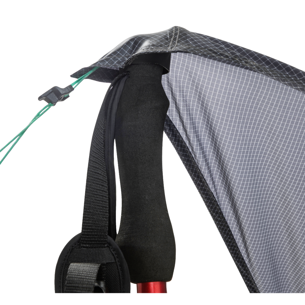 Close-up of the Big Agnes String Ridge VST 1.5, with a trekking pole supporting the tent’s black and gray fabric corner, black strap, and green guyline with a plastic tensioner in this ultralight shelter setup.