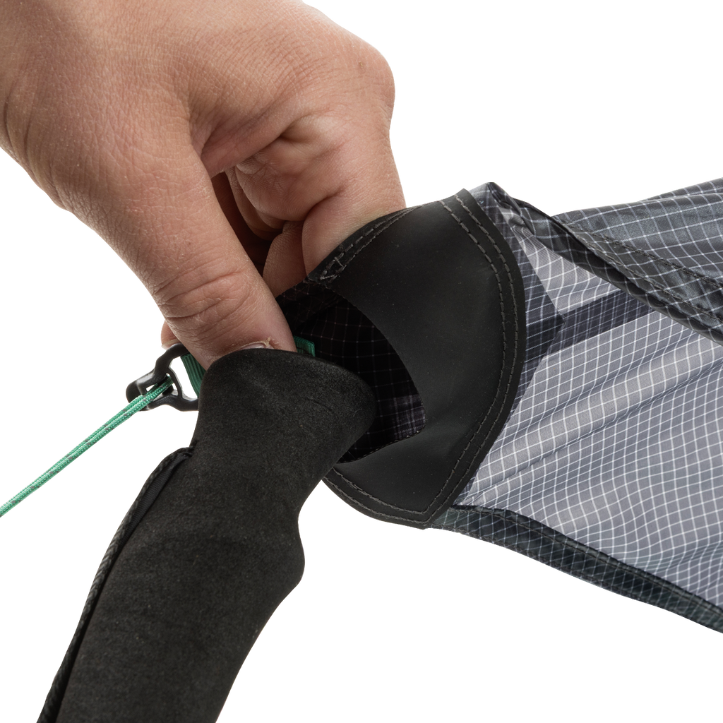 A close-up of a hand tying a green string to the end of the black and gray String Ridge VST 1.5 by Big Agnes Returns, highlighting its detailed fabric and handle—ideal for assembling ultralight shelters or VST tents on your outdoor trips.