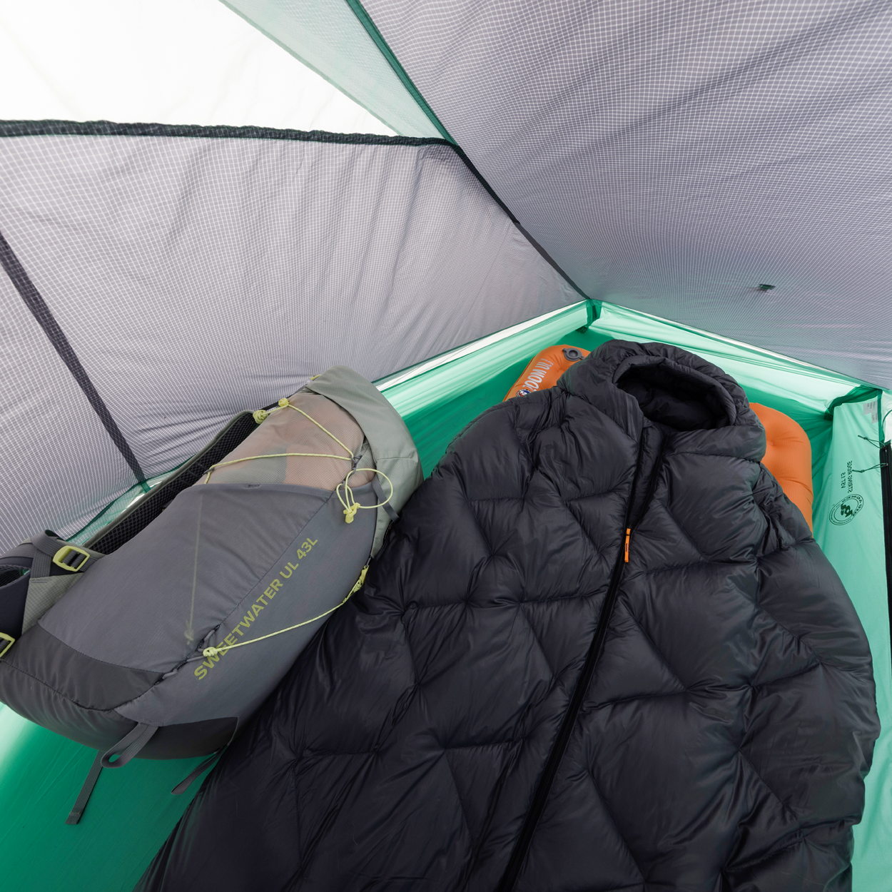 A sleeping bag and gray backpack are inside a light green Big Agnes Returns String Ridge VST 1.5 tent. Its mesh roof and sides are visible, with a sleeping pad beneath the bag—making this ultralight tent perfect for outdoor adventures.