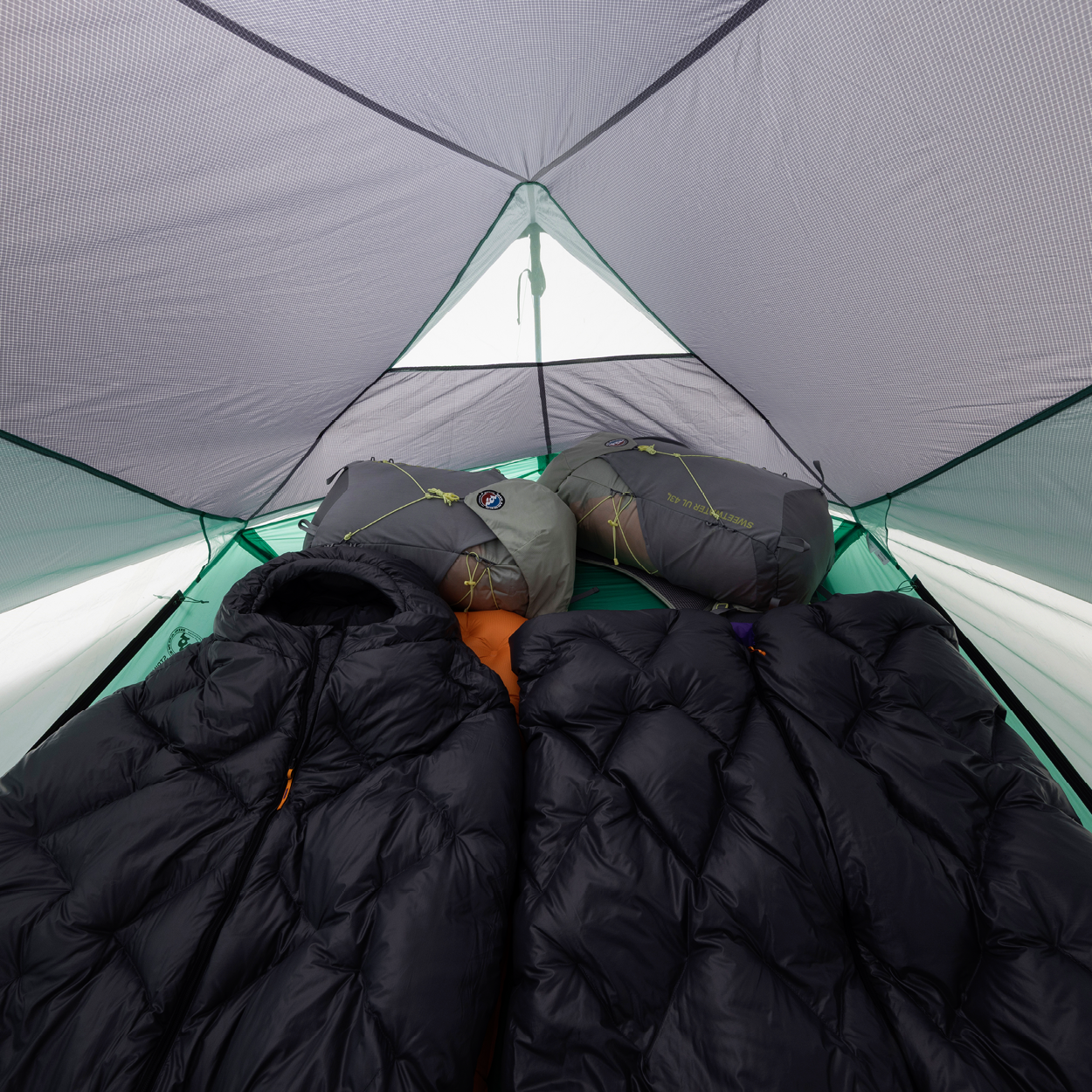 Person lying inside a tent with sleeping bags and a black quilt